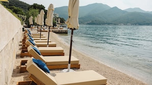 A row of sun loungers with umbrellas on a pebble beach, overlooking a calm lake with mountains in the background. - Boutique Hotel and Spa Blanc & Bleu - Blanche (Bijela)