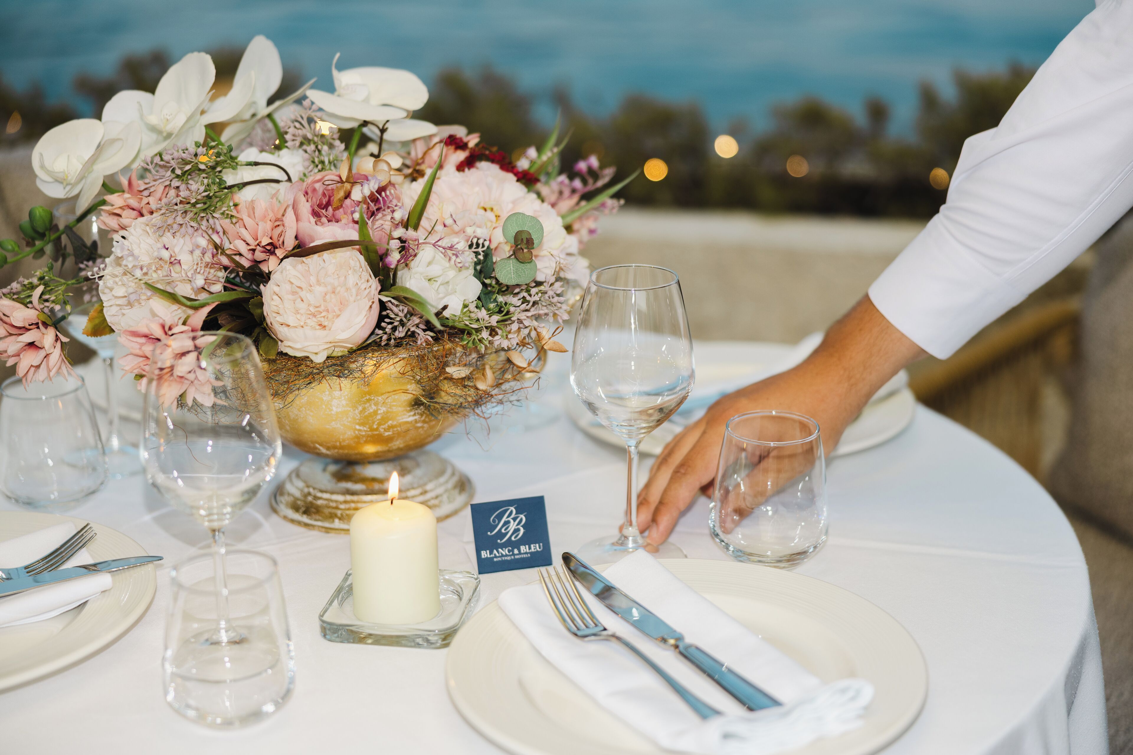 A table set with a candle, a glass bowl with flowers, and a name card.