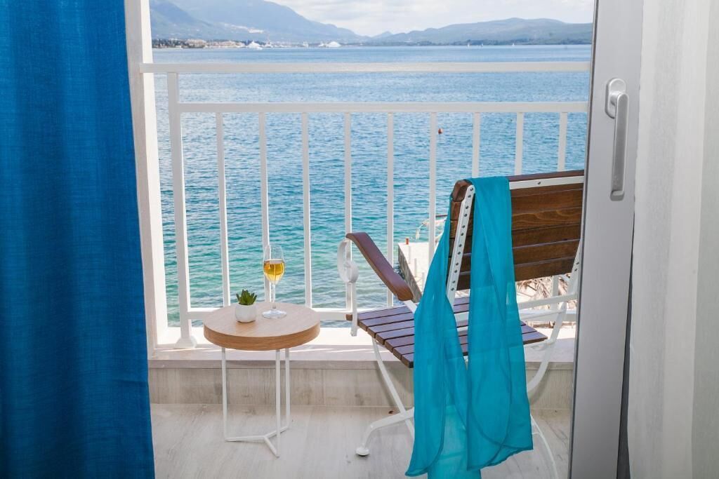 En balkon med udsigt over havet, et bord med et glas vin og en stol med et blåt håndklæde.