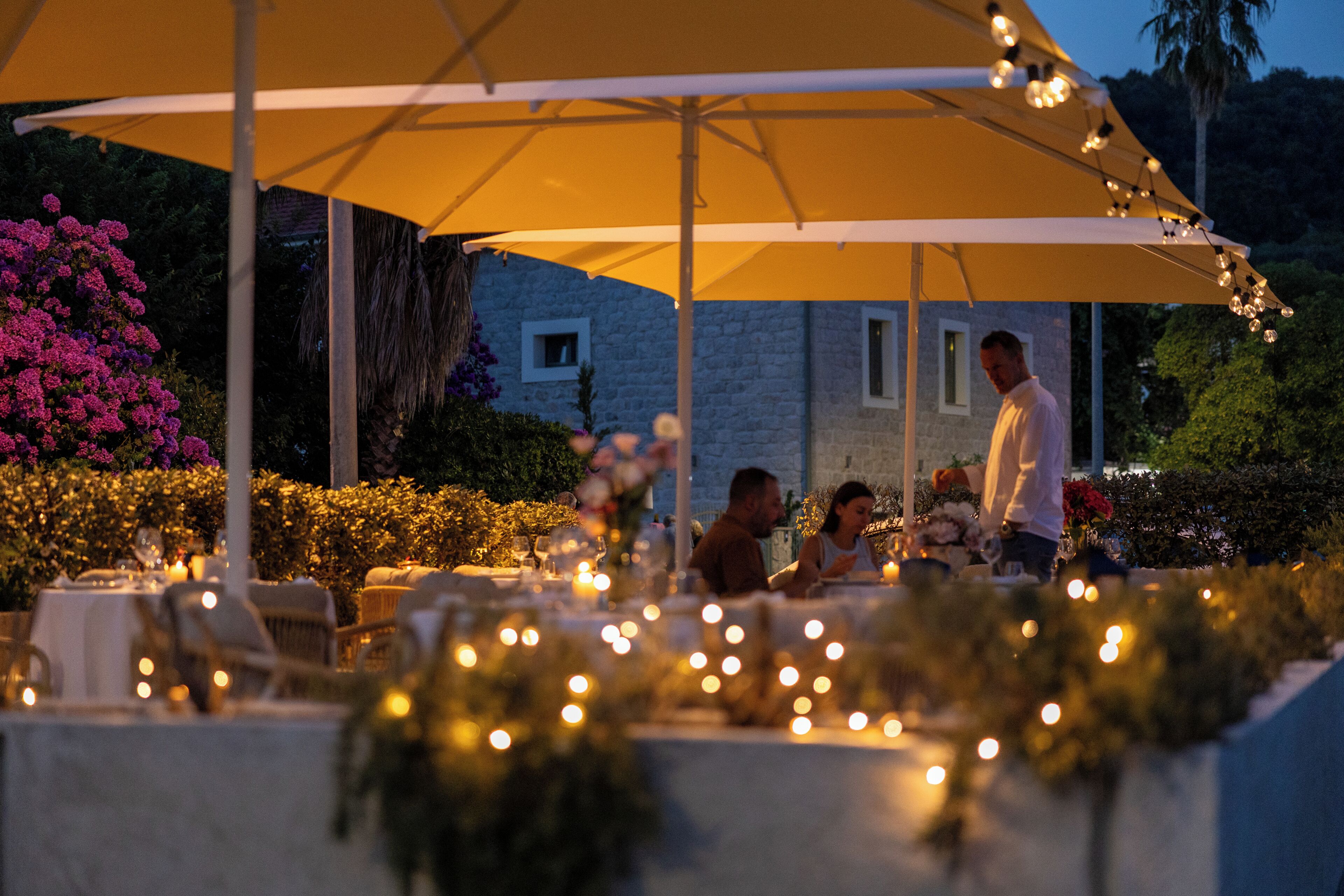 Een terras met tafels, stoelen en lichtjes.