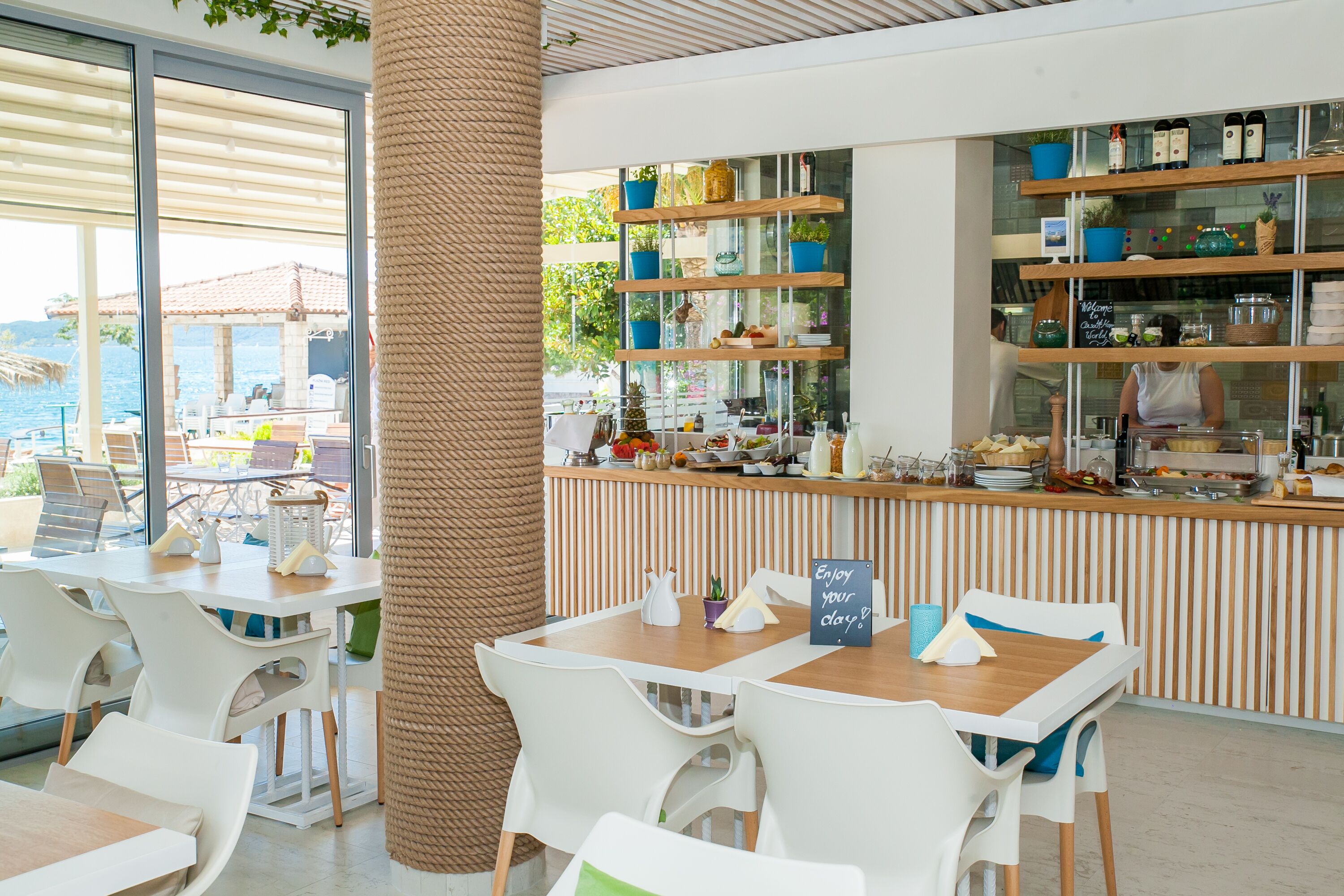 Een restaurant met een houten toonbank, witte stoelen en uitzicht op zee.