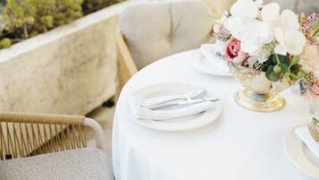Una mesa dispuesta para comer, con platos blancos, cubiertos y un centro de mesa con flores.