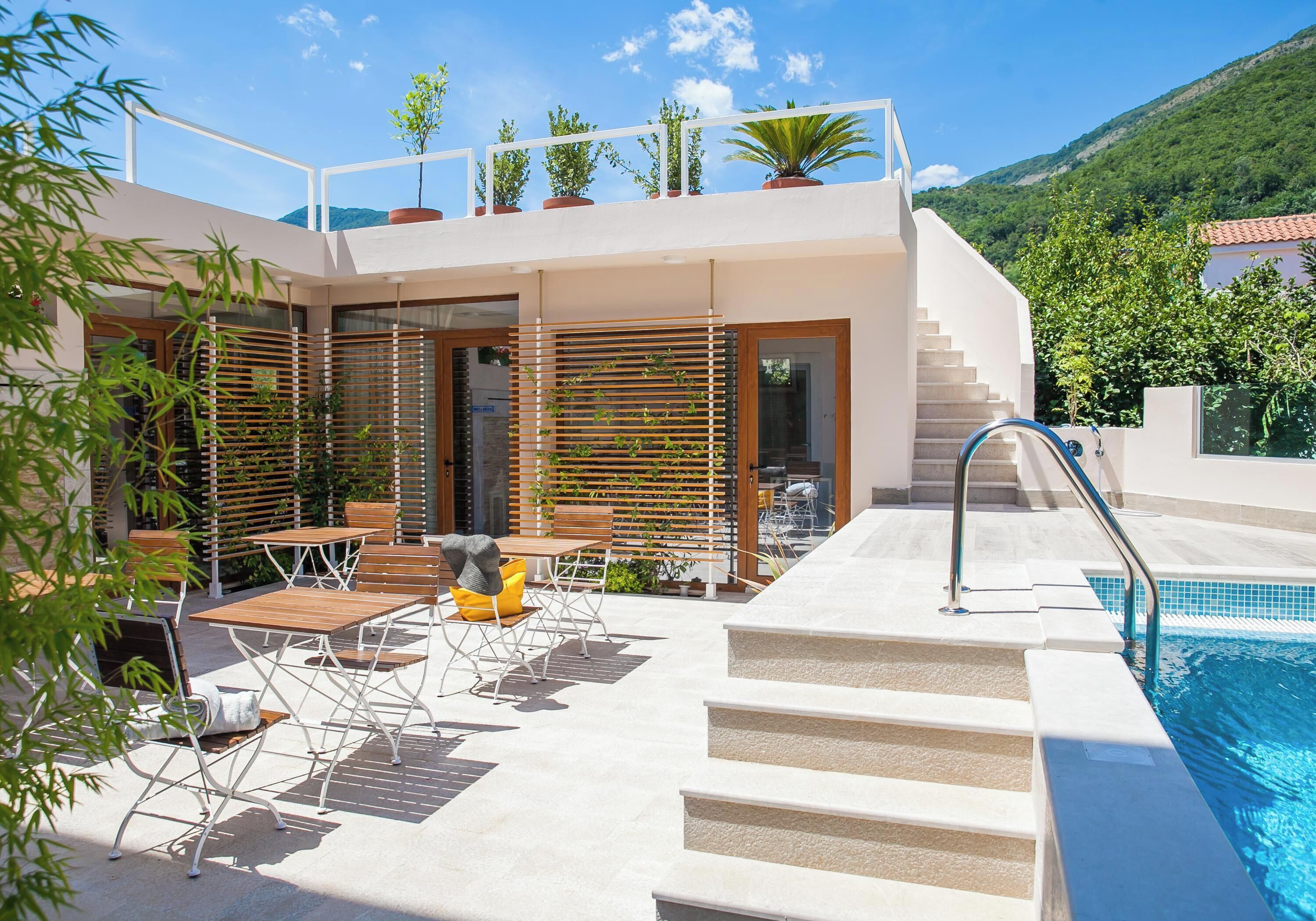 A modern outdoor pool area with steps leading to a terrace, surrounded by potted plants and wooden furniture.