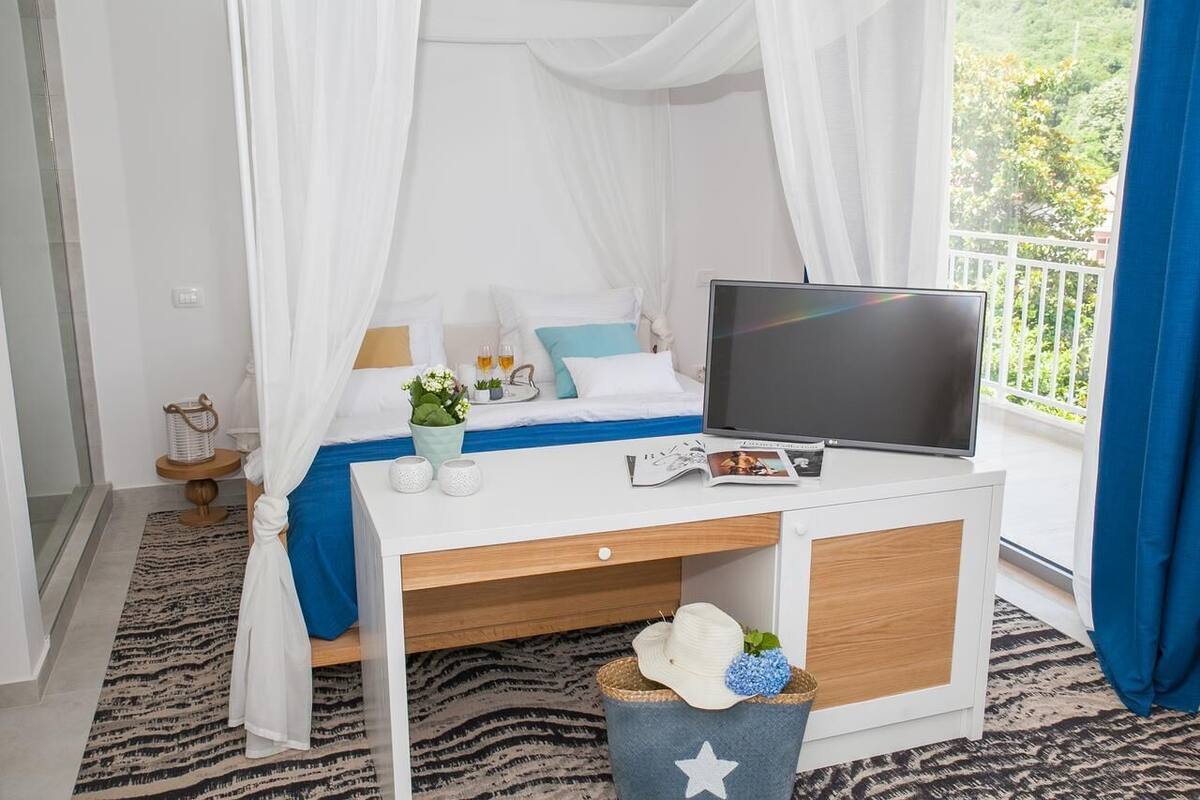A bedroom with a bed, a TV, a desk, and a window with curtains.
