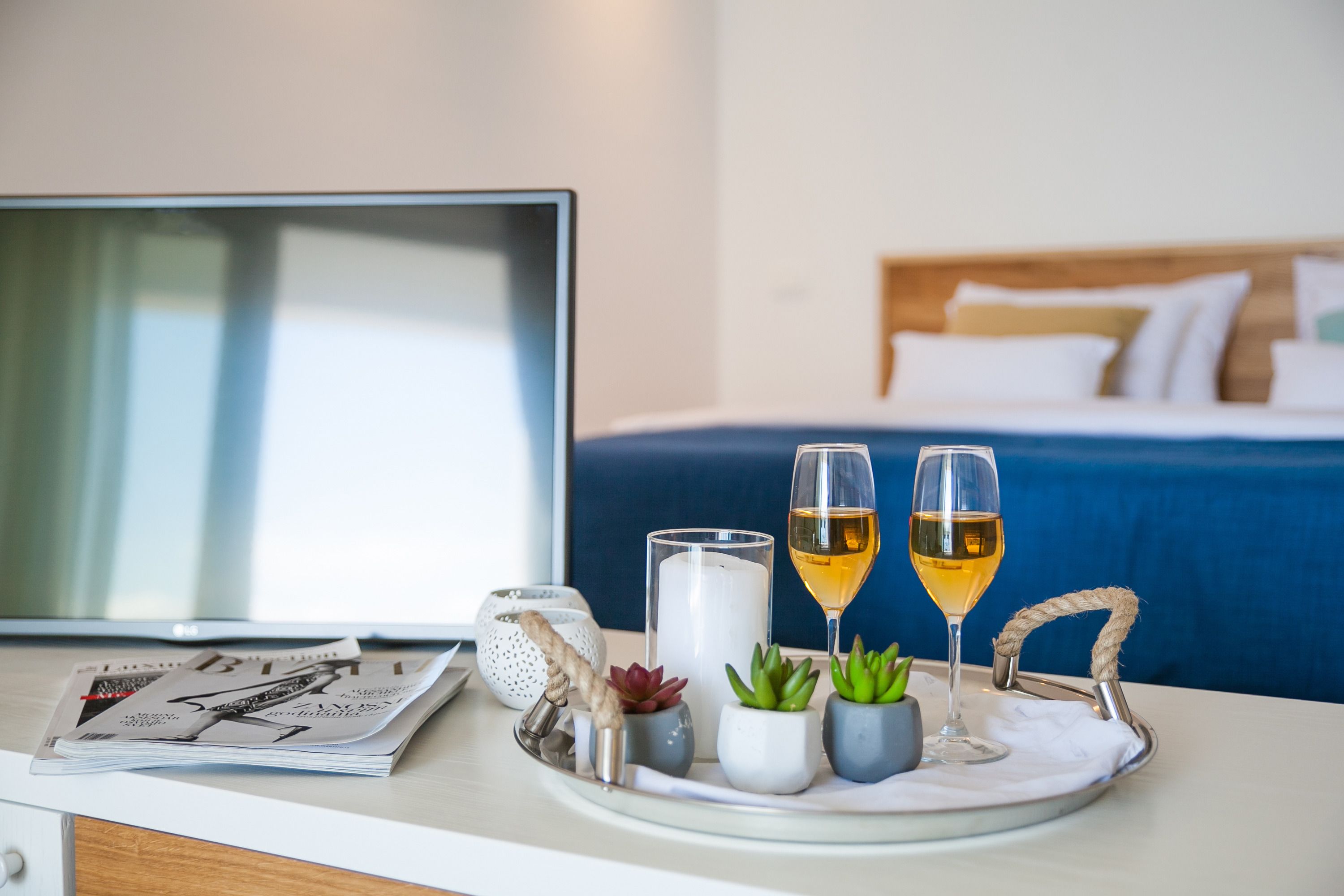 A hotel room with a bed, a TV, a tray with drinks, and a magazine.