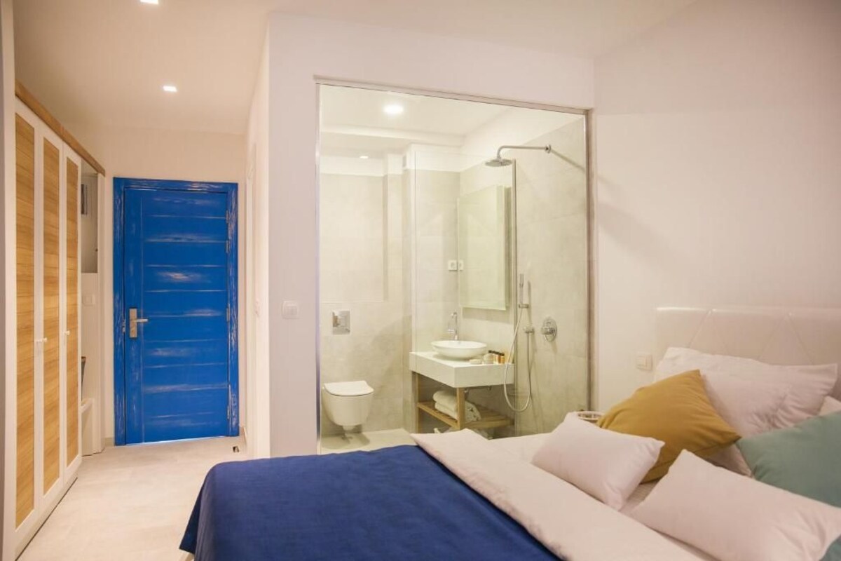 Ein Schlafzimmer mit Bett, Kissen, Nachttisch, Bad mit Dusche, Toilette und Waschbecken.