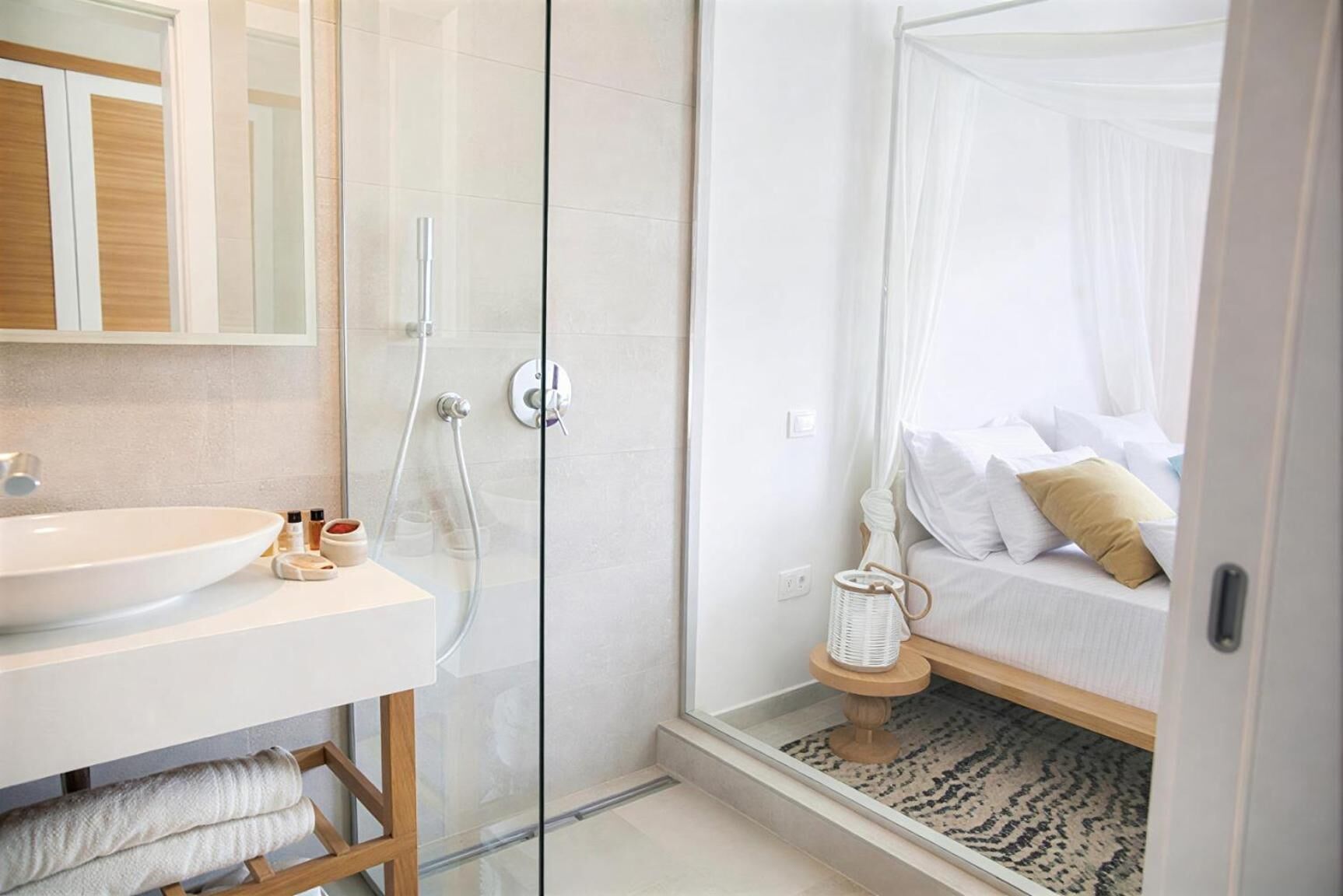 Un baño moderno con ducha de vidrio, un lavamanos y una mesita de noche con lámpara.