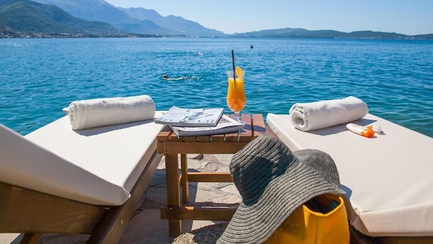 A sun lounger with a towel, a hat, and a drink on a table by a lake with mountains in the background. - Boutique Hotel and Spa Blanc & Bleu - Blanche (Bijela)