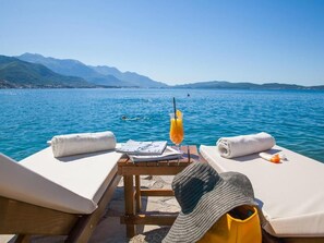 A sun lounger with a towel, a hat, and a drink on a table by a lake with mountains in the background. - Boutique Hotel and Spa Blanc & Bleu - Blanche (Bijela)