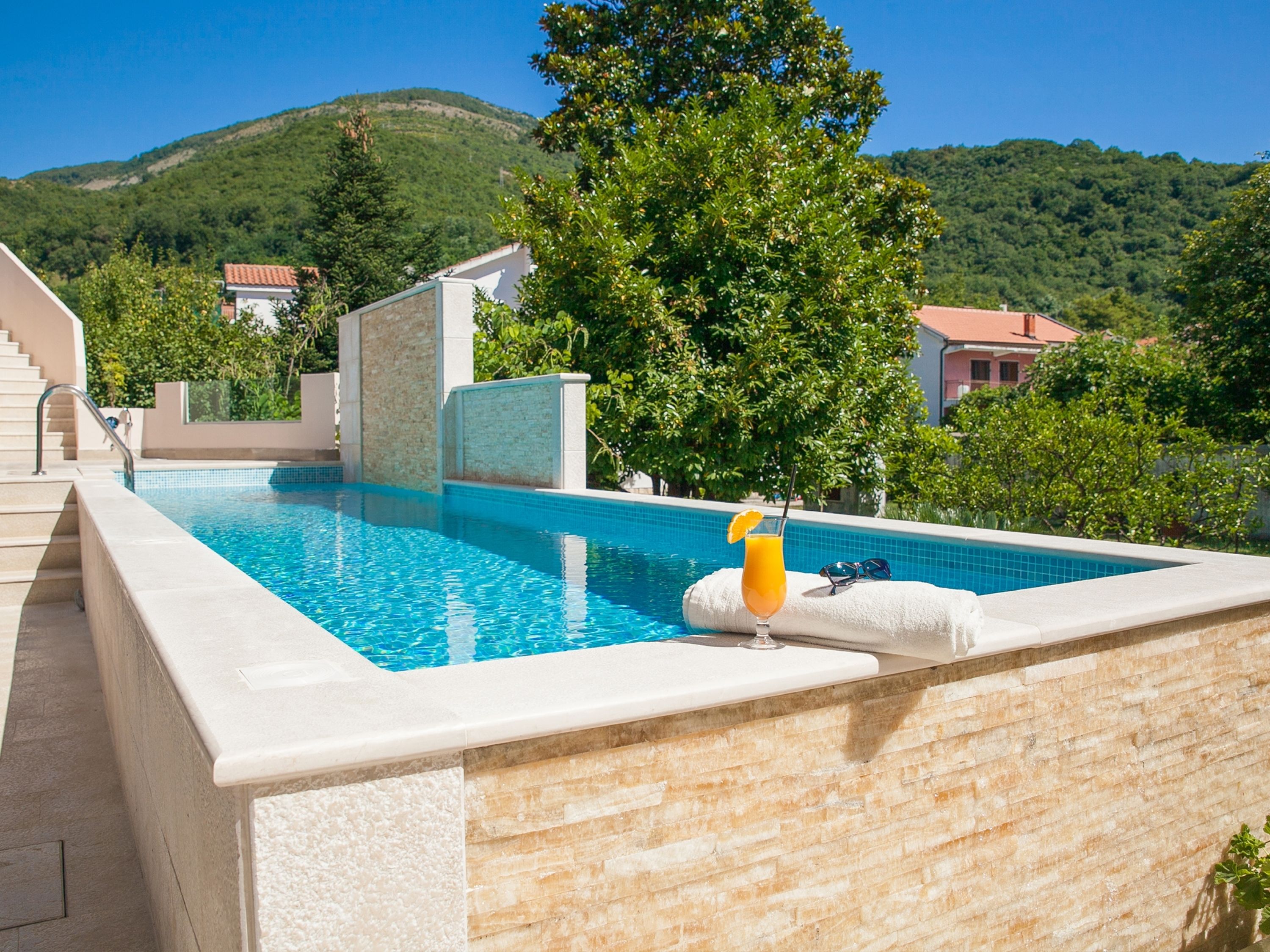 Ein Swimmingpool mit klarem, blauem Wasser, umgeben von einer Steinmauer und einem Baum.