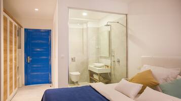 Un dormitori amb un llit, una porta blava, un bany amb plat de banyera de vidre i un lavabo blanc.