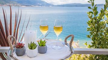 Una bandeja con dos copas de vino blanco, una vela y pequeñas macetas con plantas en un balcón con vistas al mar.