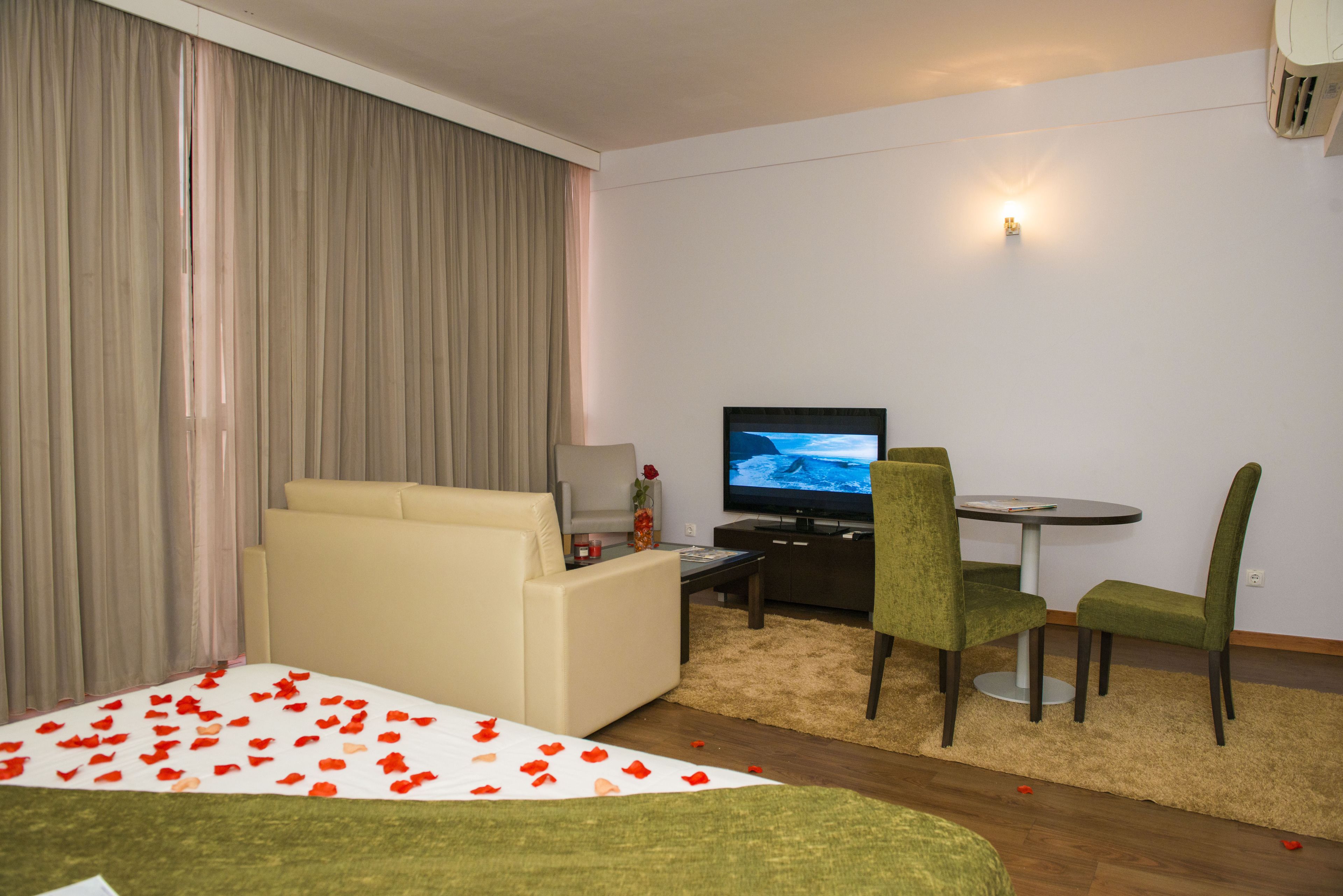 A hotel room with a bed, a sofa, a TV, a small table, and two chairs.