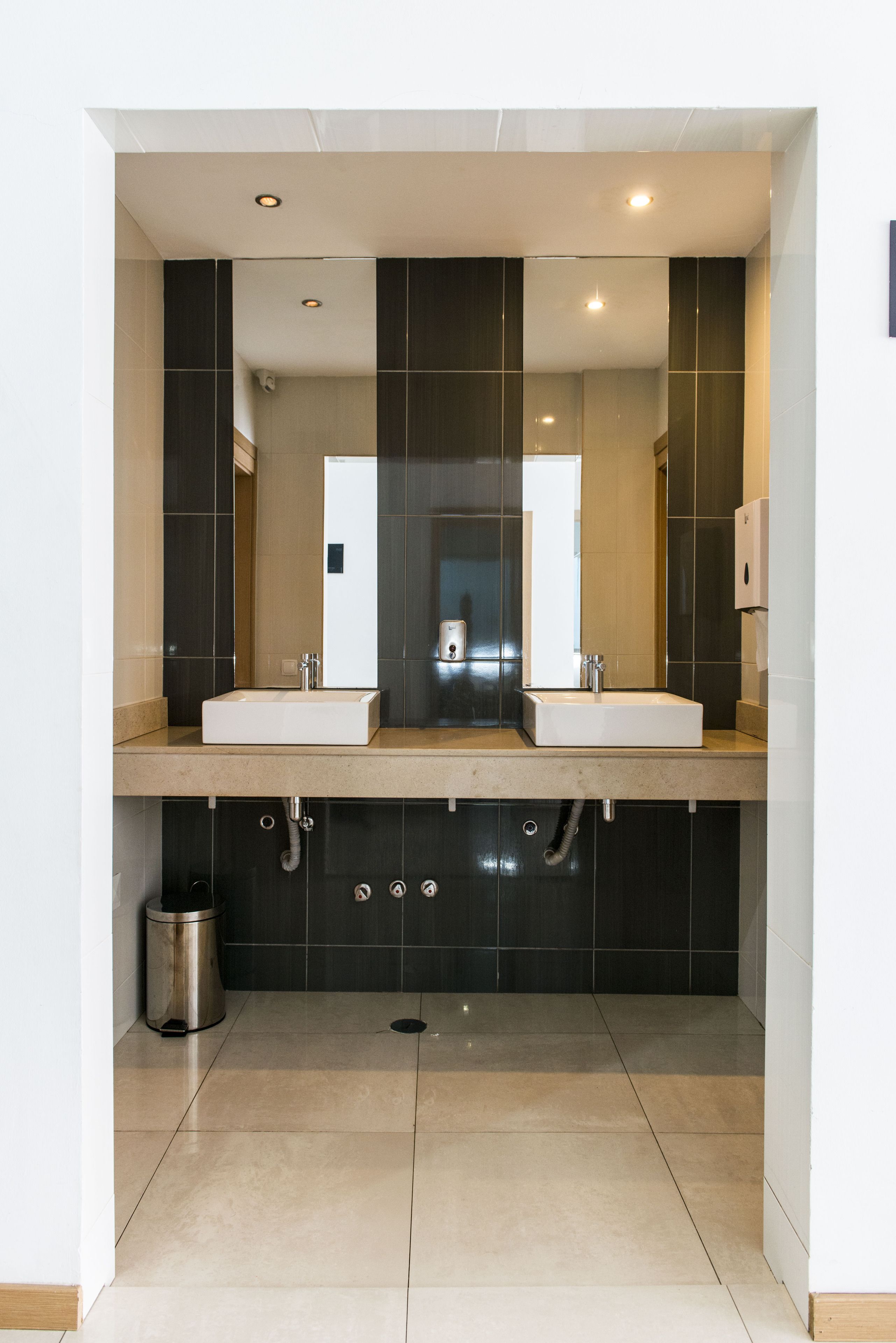 A modern bathroom with two sinks, a mirror, and a hand dryer.