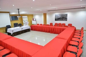 Un salón de conferencias con una larga mesa, sillas rojas, un proyector y un cartel.