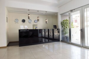 Zona de recepción de hotel con un diseño moderno, que incluye un mostrador de recepción, relojes y una planta en maceta.
