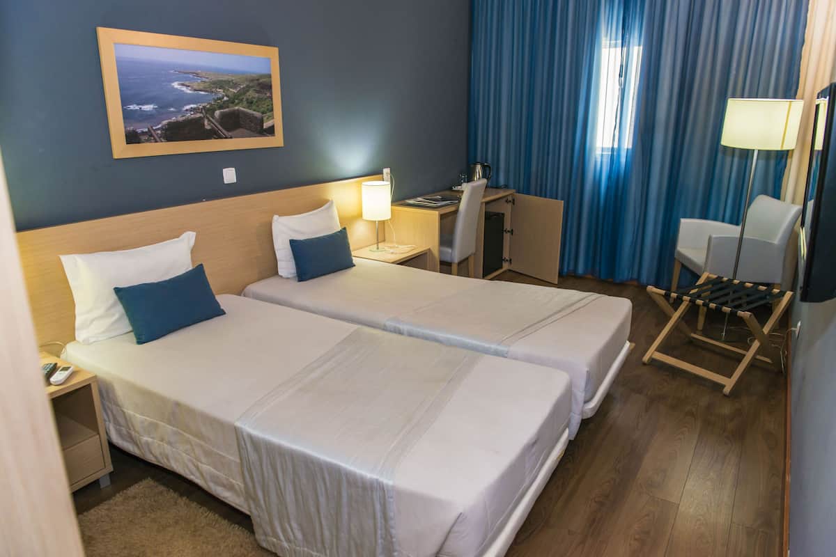 Une chambre d’hôtel avec deux lits, un bureau, une chaise, une lampe et un tableau au mur.