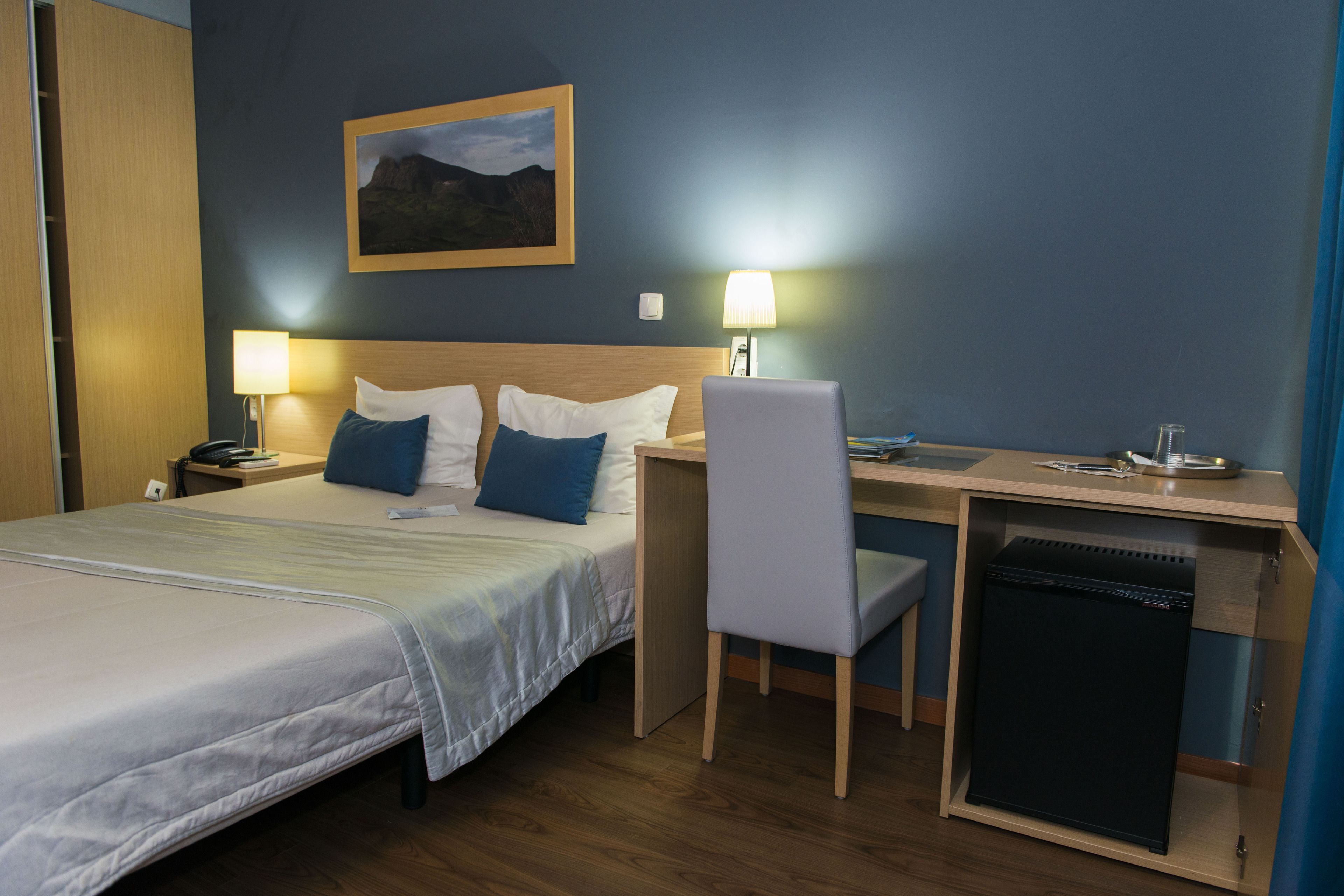 Habitación de hotel con cama, escritorio, silla y un refrigerador pequeño.