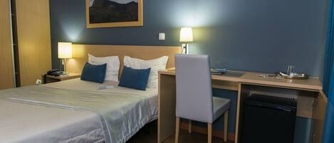 Habitación de hotel con cama, escritorio, silla y un refrigerador pequeño.