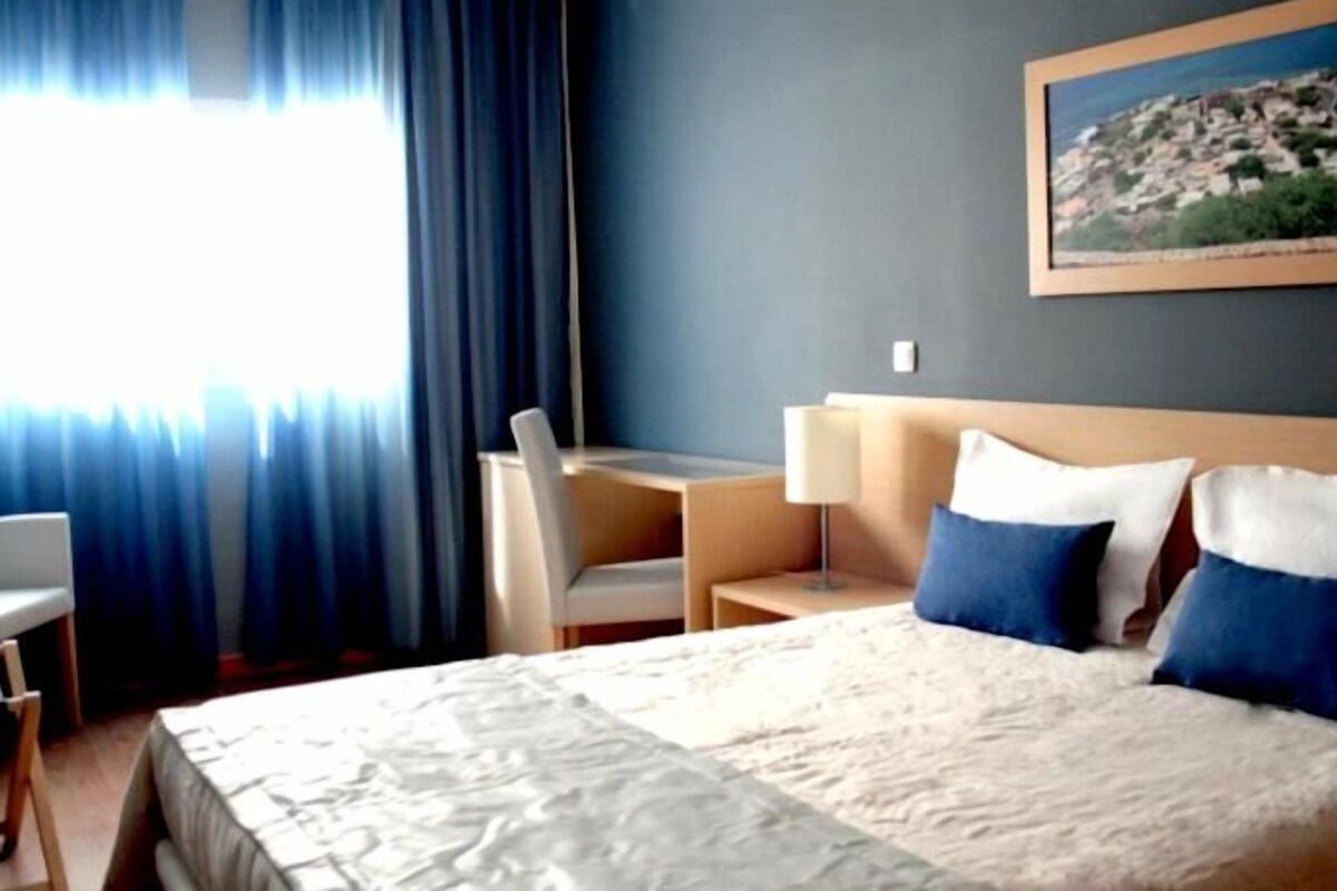 Une chambre d’hôtel avec un lit, un bureau, une chaise et un tableau au mur.