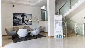 Um hall de hotel moderno com área de refeições, escadaria e um grande painel informativo.