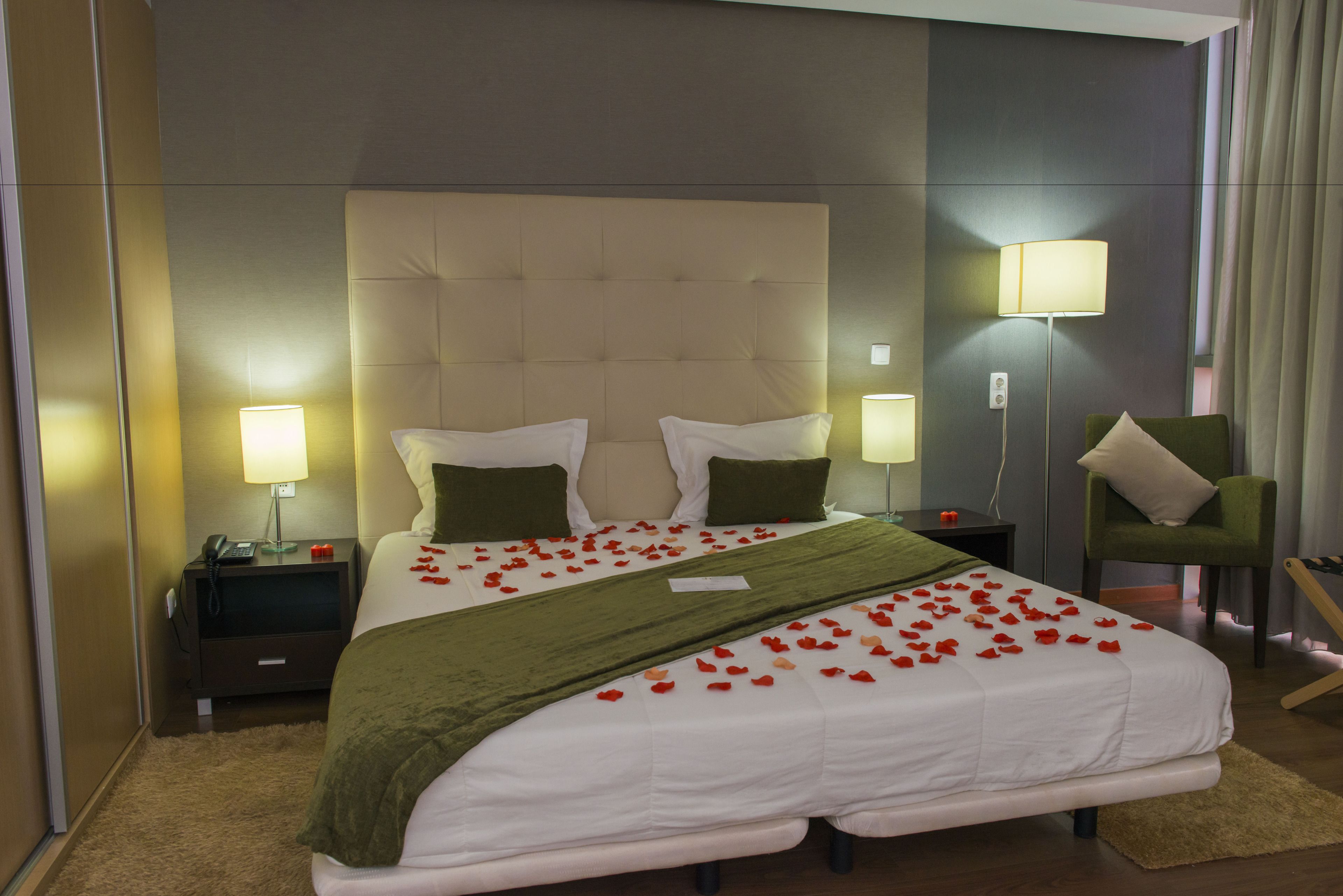 Una habitación de hotel con una cama grande, dos mesitas de noche, un sillón verde y una lámpara.