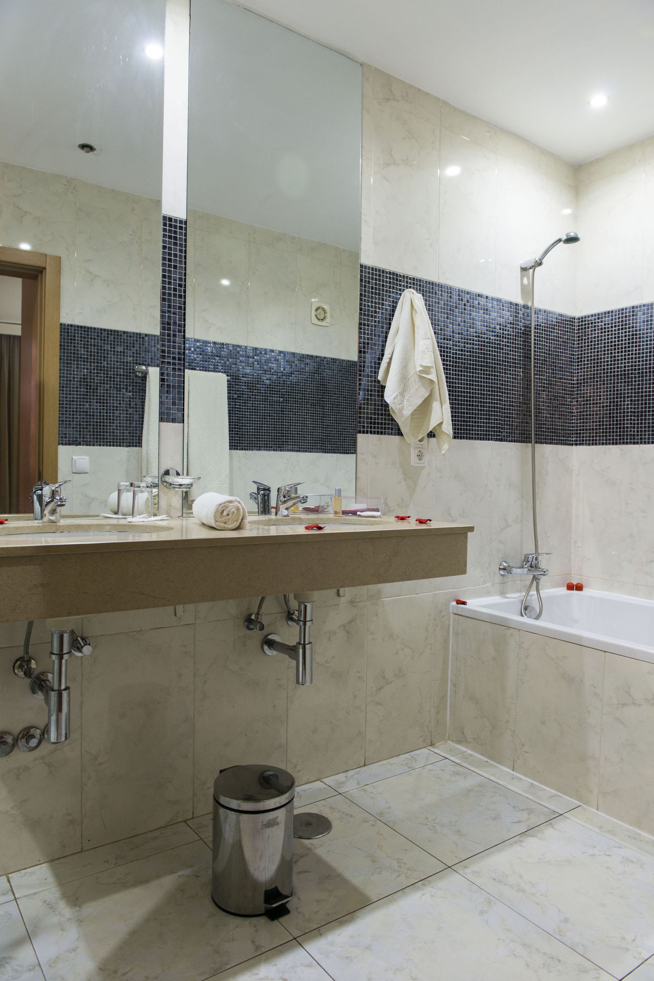 A bathroom with a large mirror, a bathtub, and a sink with a towel hanging on the wall.