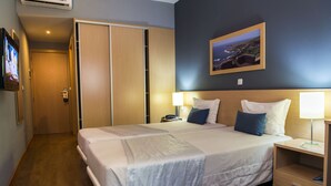 Quarto de hotel com uma cama grande, abajures, mesa de cabeceira, televisão e vista para o mar.