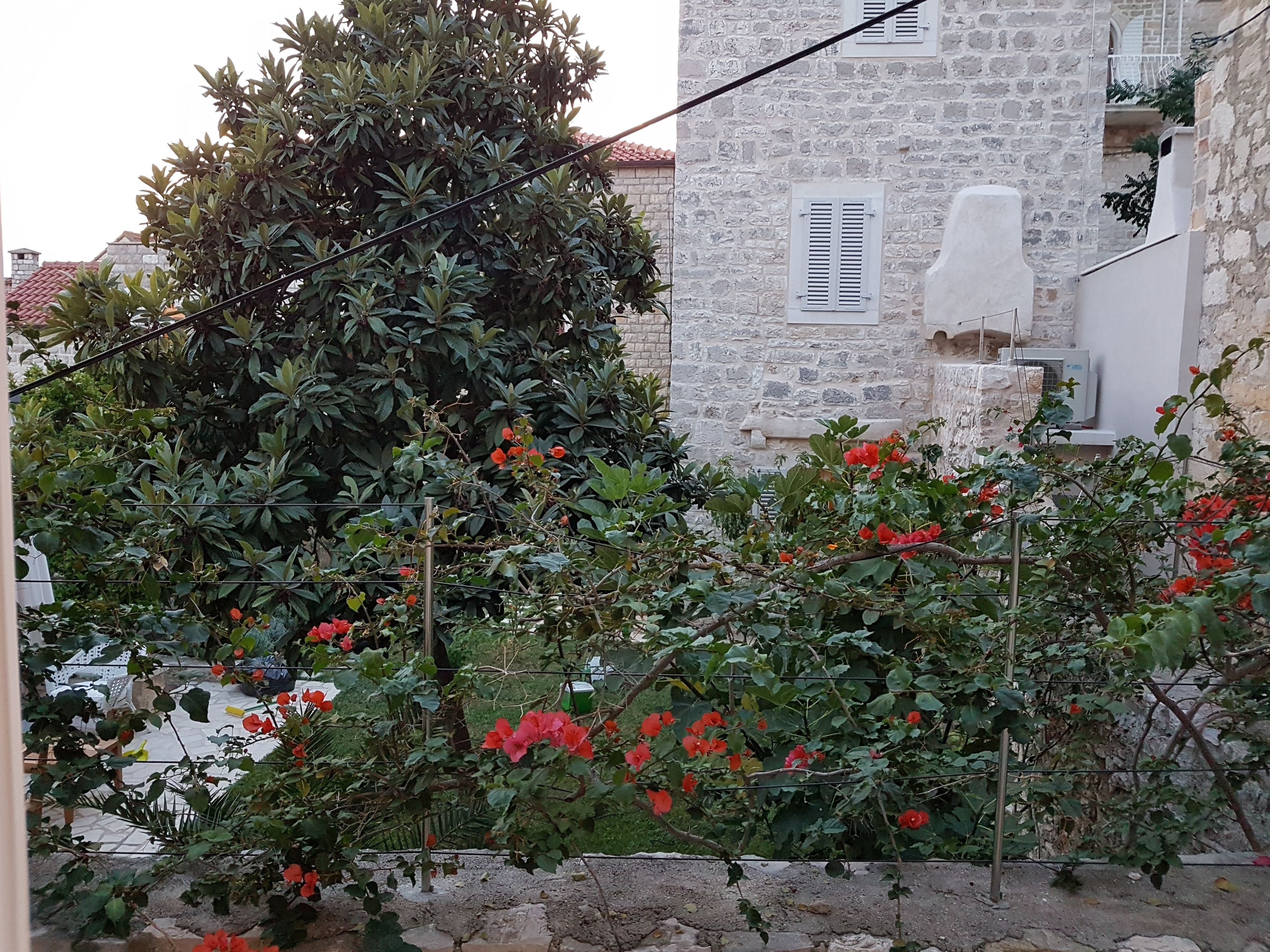Un edificio de piedra con aspecto rústico, rodeado de abundante follaje y plantas florecientes.