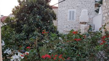 Un edificio de piedra con aspecto rústico, rodeado de abundante follaje y plantas florecientes.