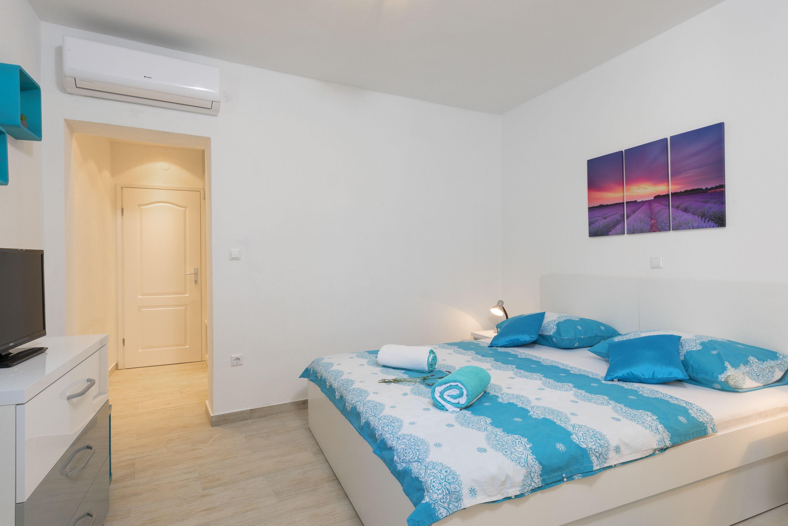A modern bedroom with a bed, a TV, and a painting on the wall.