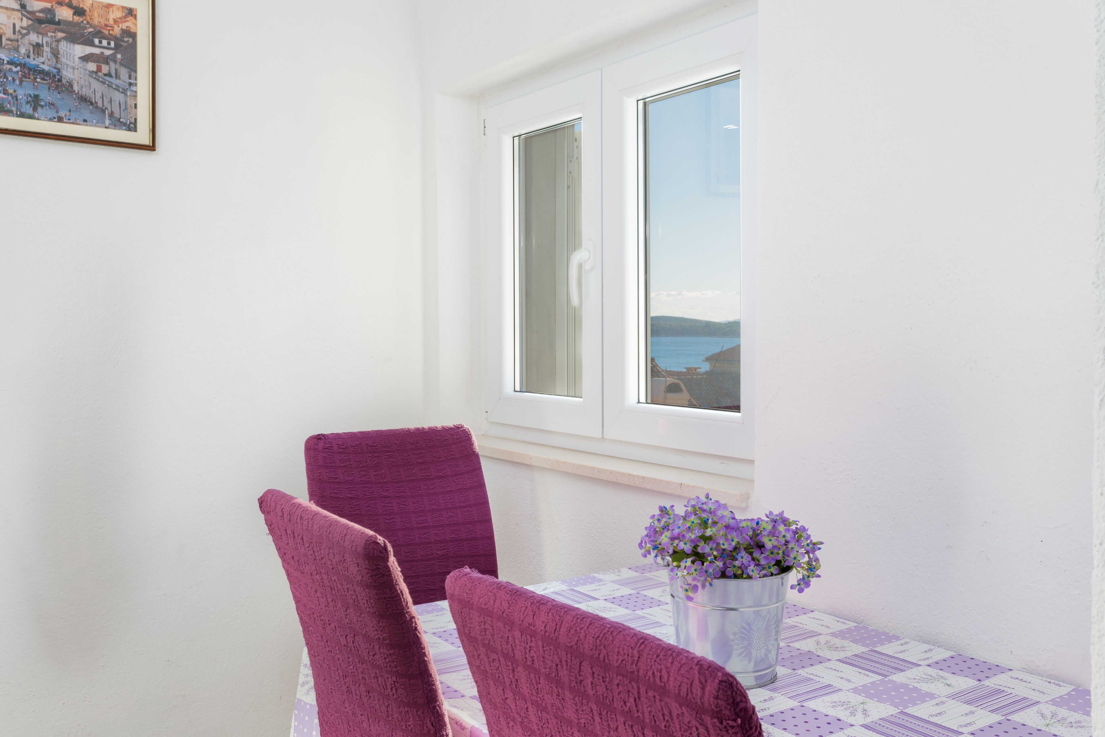 Una habitación pequeña con una mesa y dos sillas, una ventana con vista al mar y un cuadro en la pared.