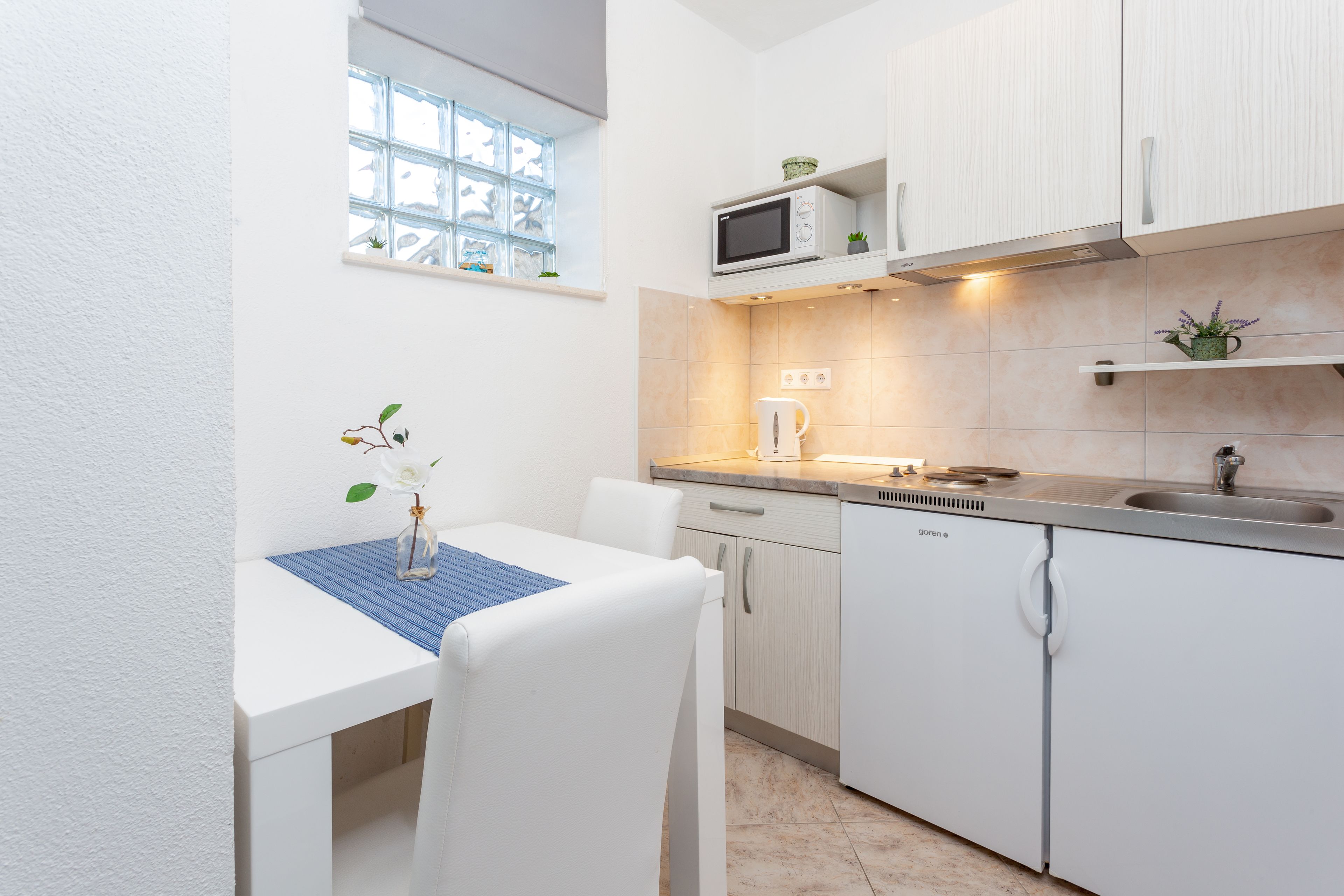 Una cocina compacta con armarios blancos, microondas, lavamanos y ventana con vistas.