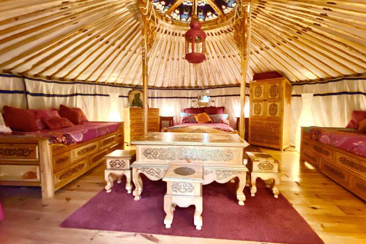 A traditional yurt interior with a central bed, two side beds, and a decorative chest.