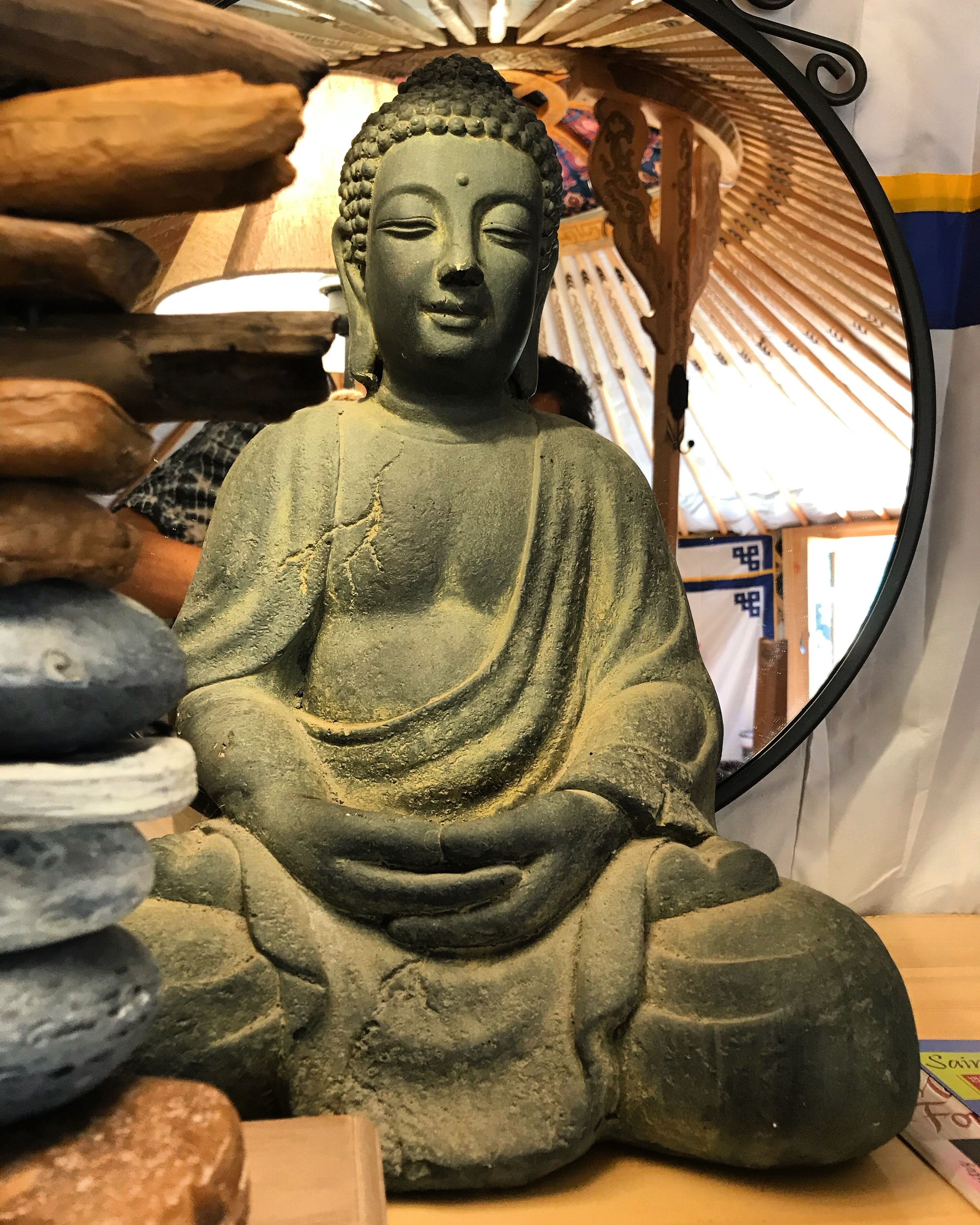 Istuva Buddha-patsas huoneessa, jossa on puinen katto ja peili, joka heijastaa osan huoneesta.