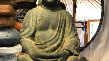Istuva Buddha-patsas huoneessa, jossa on puinen katto ja peili, joka heijastaa osan huoneesta.