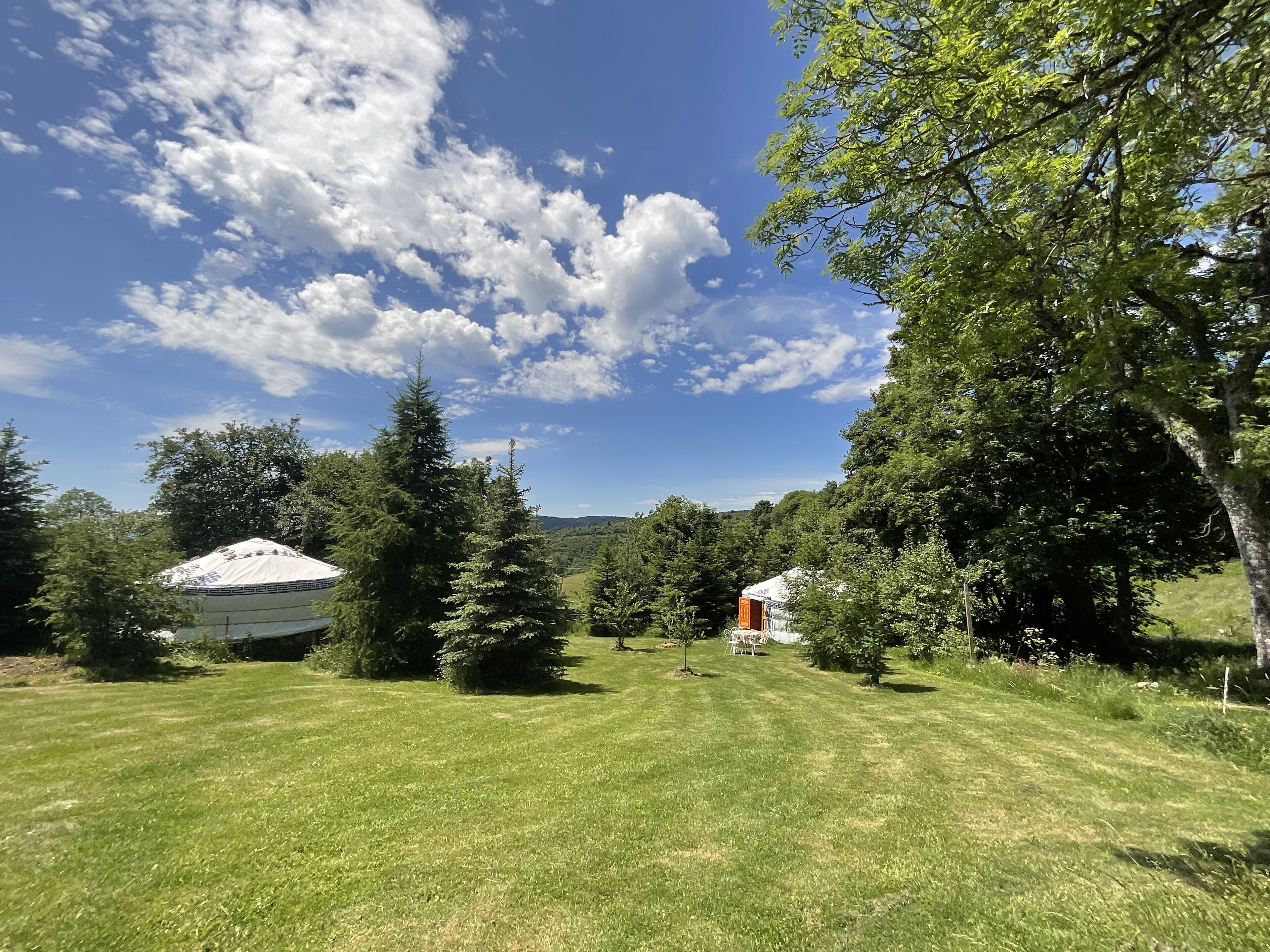A grassy field with a white tent and a small building in the distance.