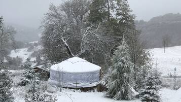 A snow-covered landscape with a tent-like structure in the foreground, surrounded by trees and a snowy hill in the background.