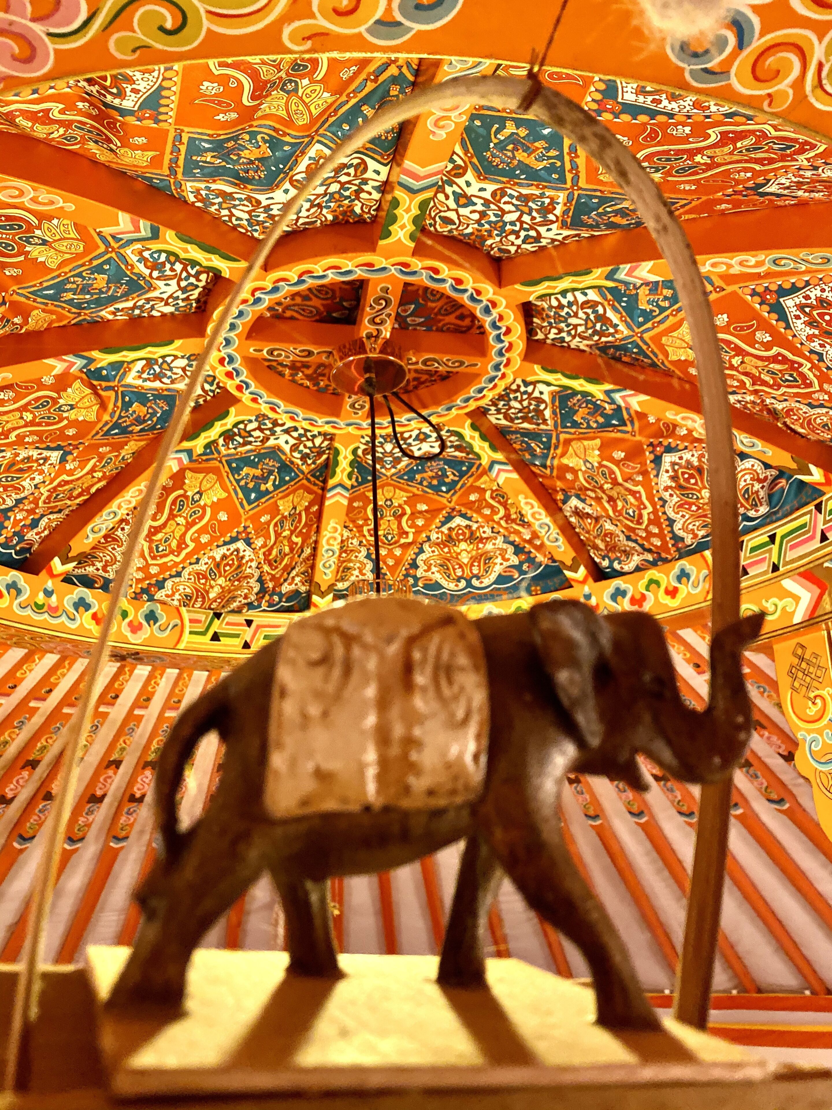 Un plafond coloré et richement décoré, orné d’un motif circulaire central et d’une sculpture d’éléphant.