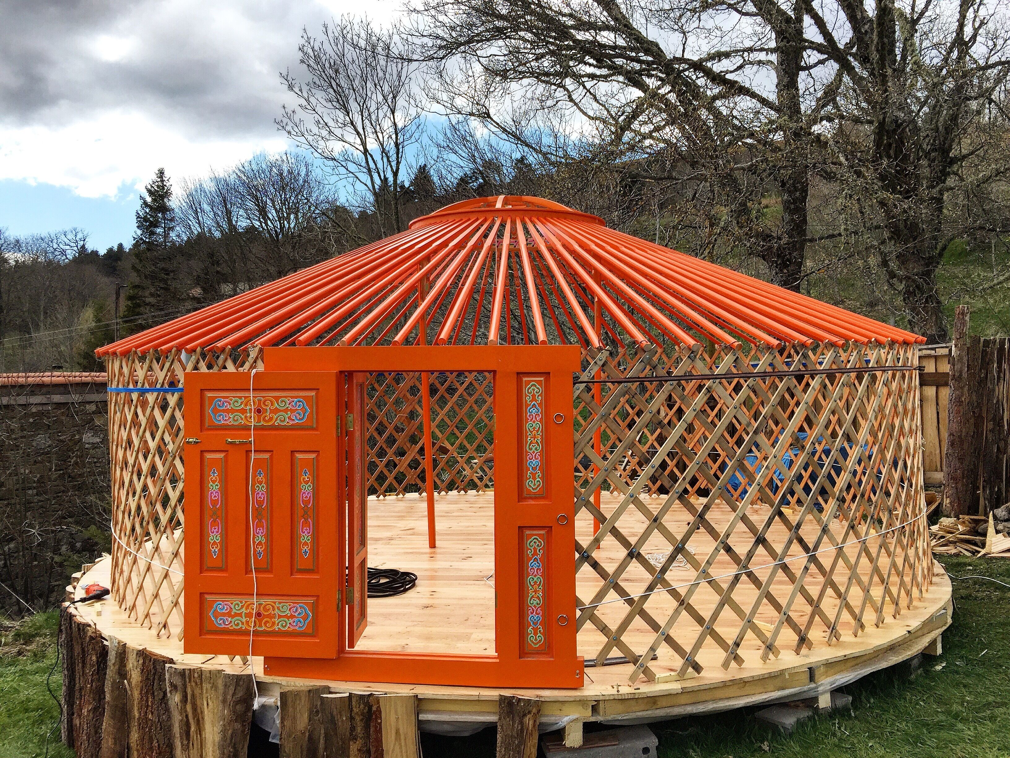 A yurt with an open door, a wooden floor, and a lattice wall.