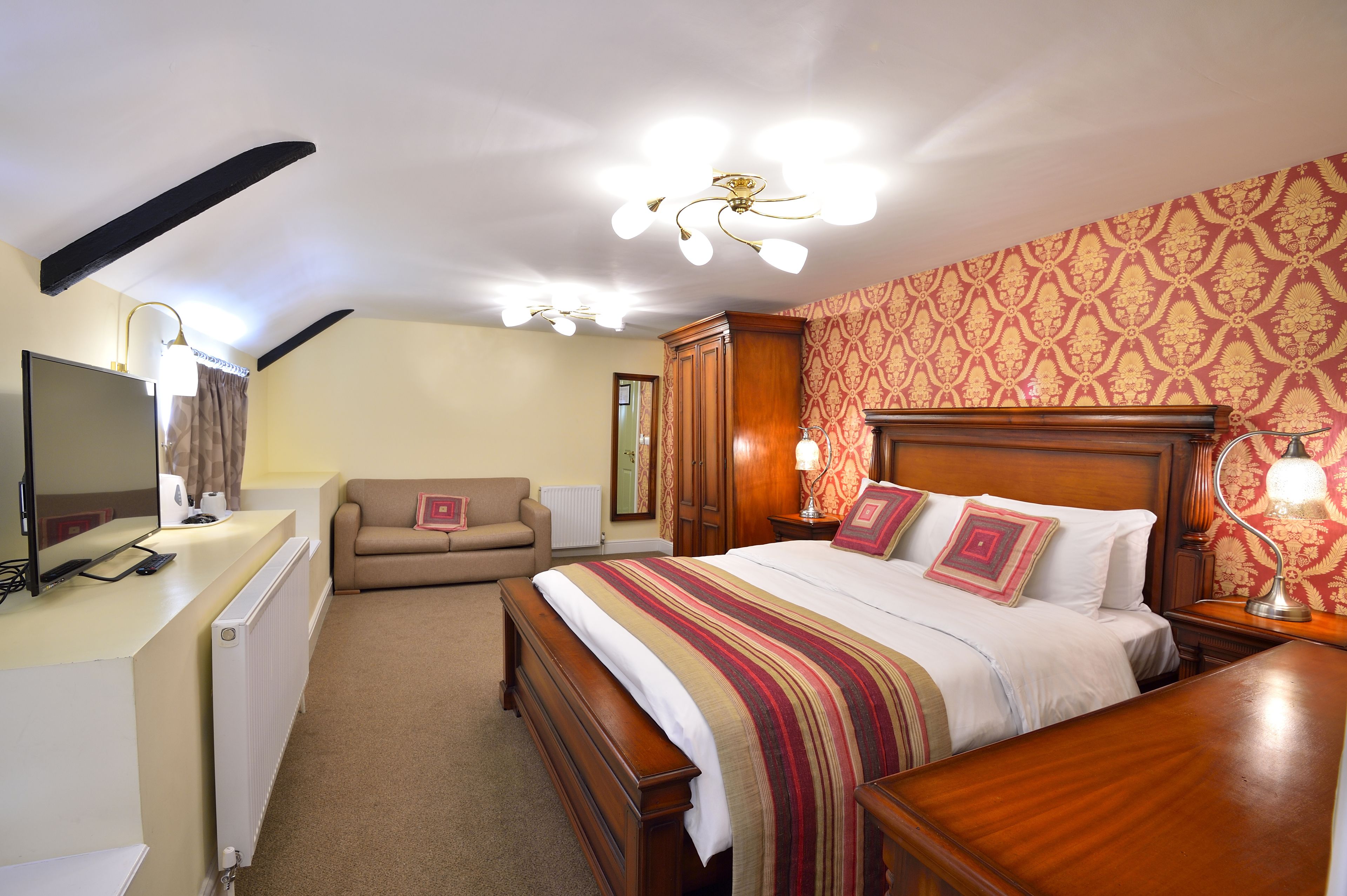 Ein Hotelzimmer mit einem großen Bett, einem Schreibtisch mit Computer, einer Sitzecke und einem Holzkopfende.