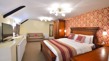 Quarto de hotel com uma cama grande, uma escrivaninha com computador, um sofá e uma cabeceira de madeira.