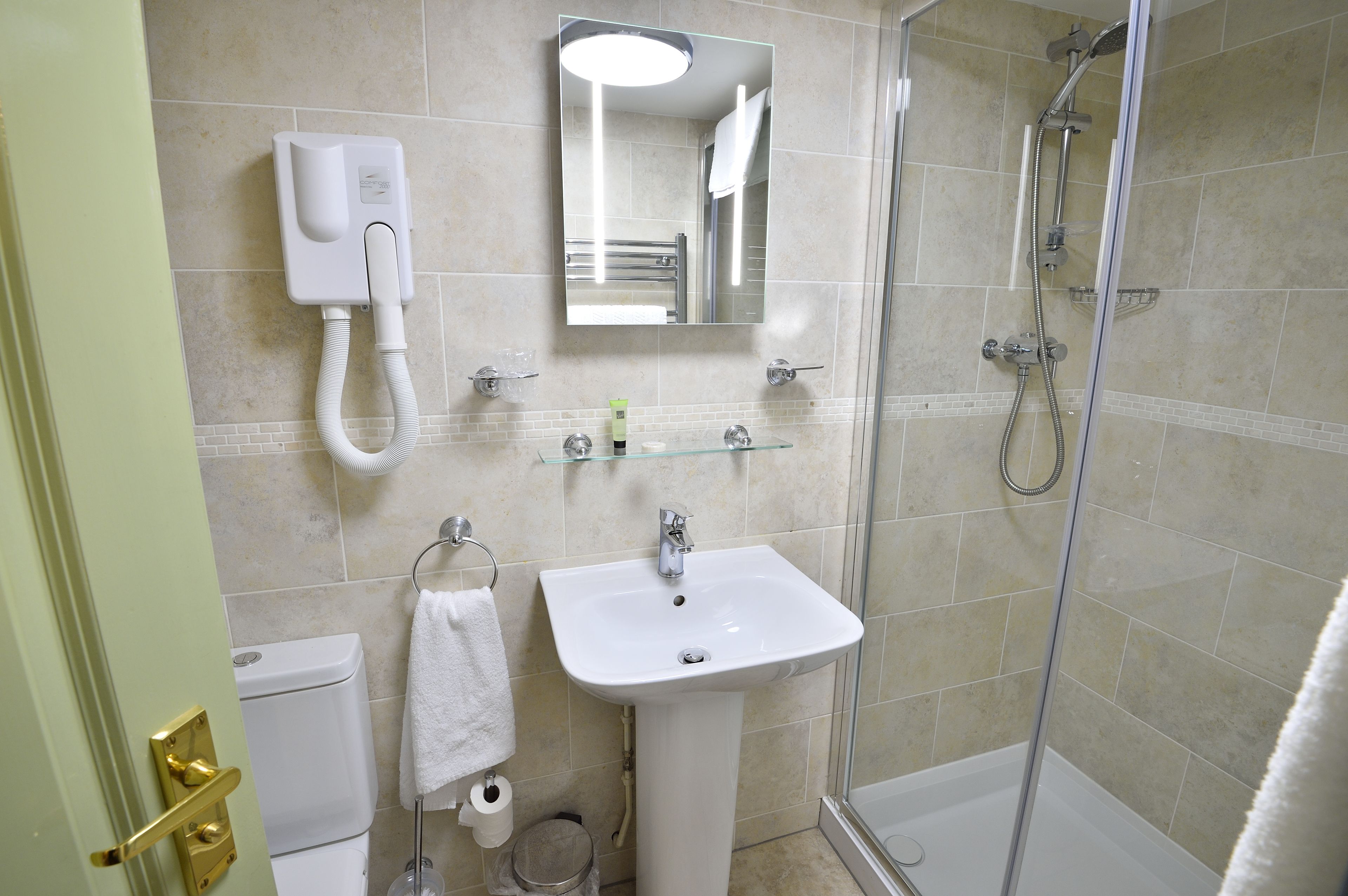 Un baño con lavamanos blanco, espejo, cabezal de ducha de mano y retrete.