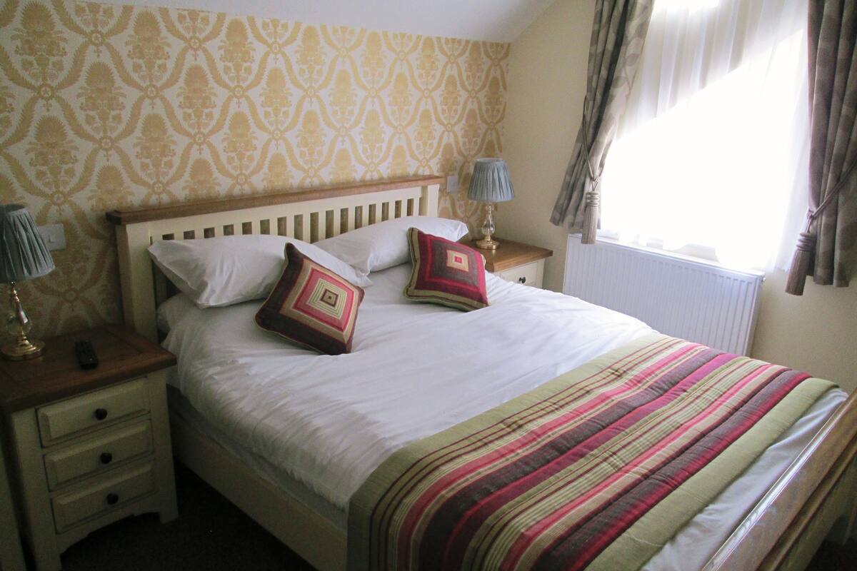 A neatly made bed with a striped blanket, two pillows, and a bedside table with a lamp.