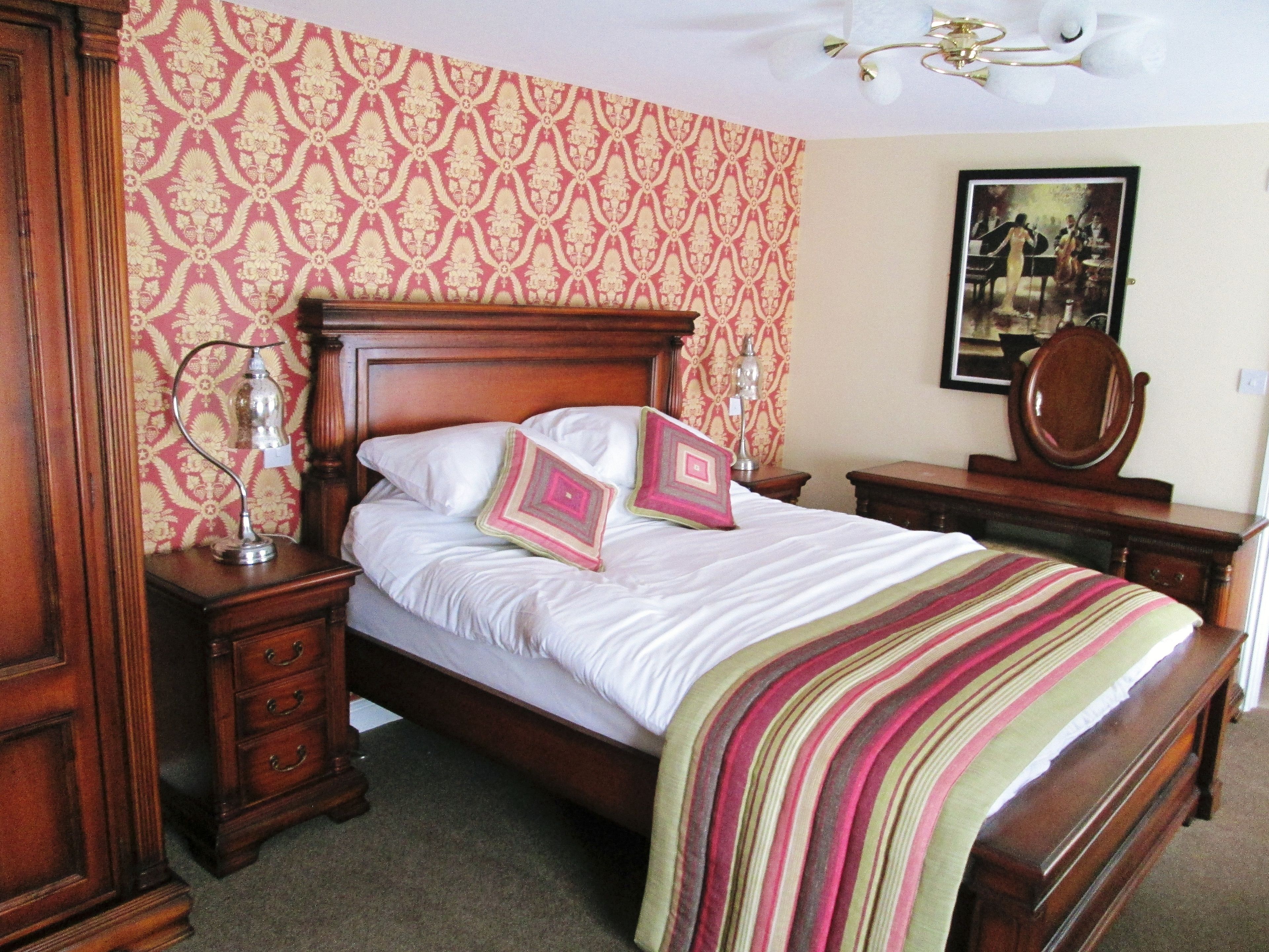 Un dormitorio con cama de madera, mesita de noche, cómoda y espejo.