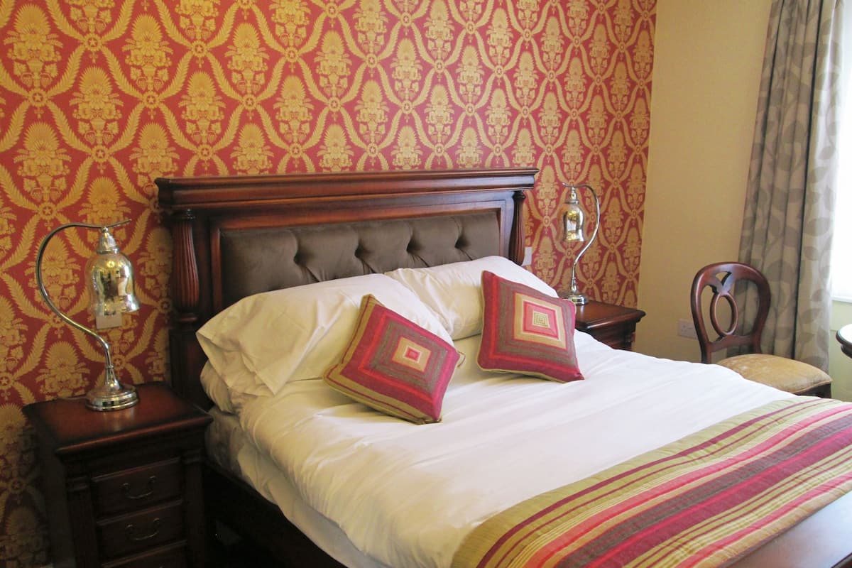 A neatly made bed with a striped blanket, two decorative pillows, a wooden nightstand with a lamp, and a chair.