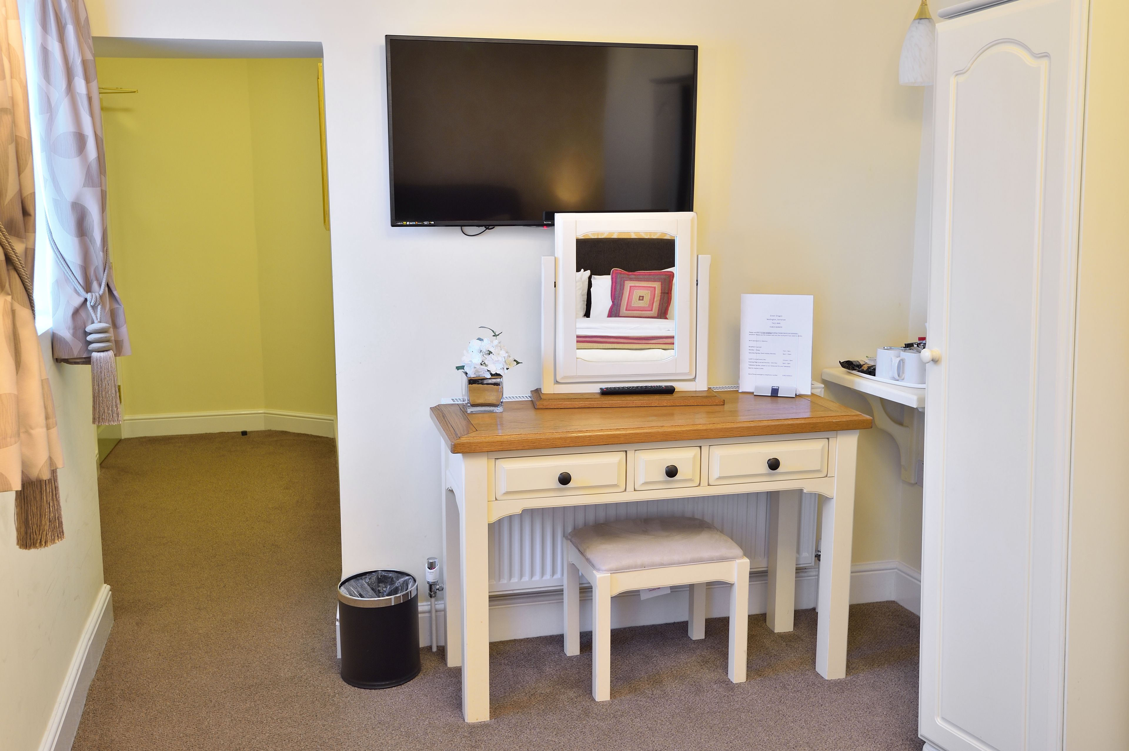A compact room with a wooden desk, a television, a small bench, and a radiator.