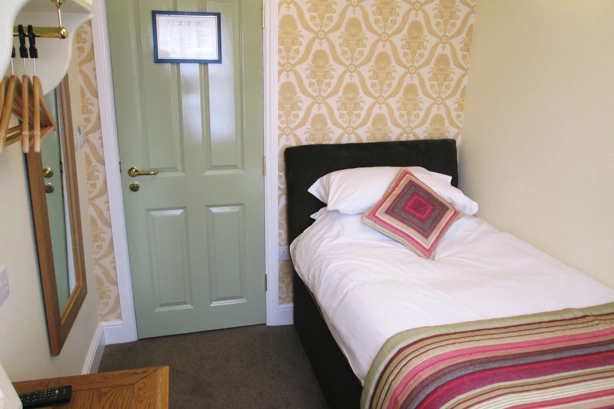 A hotel room with a bed, a door with a sign, a mirror, and a carpeted floor.