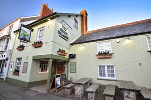 Un pub tradicional con fachada verde, bancos de madera afuera y un letrero que anuncia 'The Green Dragon Accommodation'.