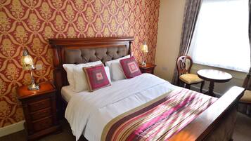 A neatly made bed with a striped bedspread, two bedside lamps, a wooden nightstand, and a chair by a window with curtains.